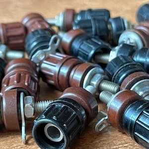 May include: A close-up of a pile of brown and black electrical terminal connectors. The connectors have a threaded metal post and a screw-on cap. They are used to connect wires to electrical components.