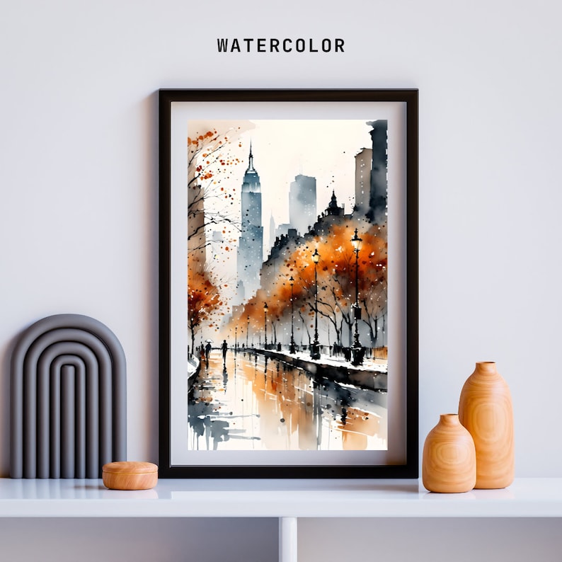 May include: A watercolor painting of a city street scene with tall buildings, trees with orange leaves, and people walking on a sidewalk. The street is wet from rain and reflects the buildings and trees. The painting is framed in black.