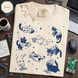 May include: Ivory-colored Comfort Colors t-shirt featuring navy blue cartoon cats with laptops, keyboards, and other tech accessories. The shirt has the text "Hack Planet" and "Linux". The shirt is size XL 78-20.
