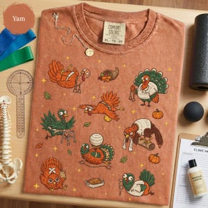 May include: A rust-colored t-shirt featuring a graphic print of various cartoon turkeys in different poses and activities, including one with a walker, one with a cornucopia, and one with a bandage. The shirt has a crew neck and a Comfort Colors label.