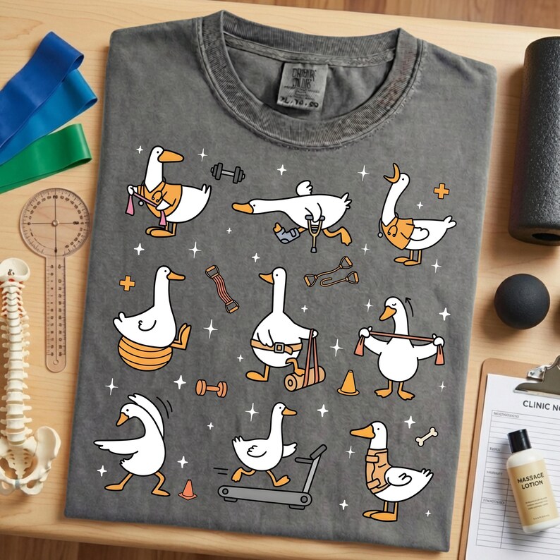 May include: Dark gray t-shirt featuring cartoon ducks engaged in various physical therapy exercises. The ducks are depicted with orange accents and are using weights, treadmills, and resistance bands. The shirt includes the text "Urban Wear" on the tag.