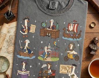 May include: Gray t-shirt featuring cartoon geese in historical and cultural costumes. The geese are depicted as historical figures, including a Viking, an Egyptian pharaoh, and a president. The shirt has the text "XL TG 50" on the tag.