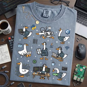 May include: A light blue t-shirt featuring cartoon geese in hoodies, each depicted with coding-related tools like laptops and servers. The shirt includes the text "CODE FUEL" on a mug and "deploy" on the shirt. A necklace and glasses are also visible.