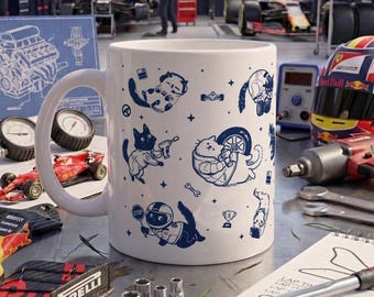 Könnte beinhalten: Ein weißer Keramikbecher mit einem wiederkehrenden blauen Grafikmuster aus Cartoon-Katzen, die als Renn-Boxencrew gekleidet sind, inklusive Katzen mit Reifen, Werkzeugen und Helmen, umgeben von kleinen Sternsymbolen und Rennmotiven.