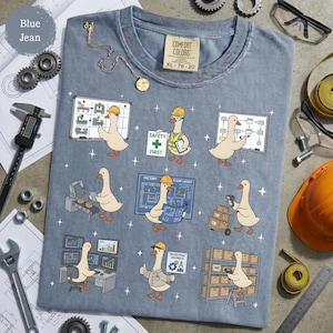 May include: Blue jean Comfort Colors t-shirt with a graphic of cartoon geese in construction worker attire. The geese are shown working on blueprints, using computers, and carrying boxes. The shirt has the text "SAFETY FIRST" and "INDUSTRIAL ENGINEER".