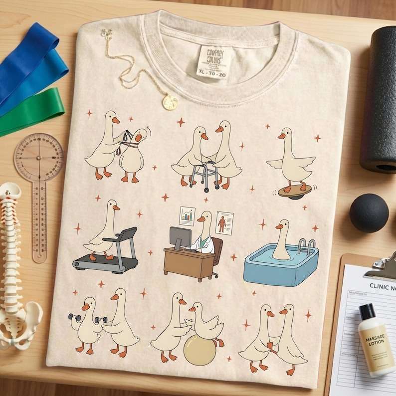 Pode incluir: Camiseta creme Comfort Colors XL 70-20 com gansos de desenho animado em v&aacute;rios cen&aacute;rios de fisioterapia. A camisa inclui gansos usando uma esteira, halteres e uma prancha de equil&iacute;brio. Um colar de ouro est&aacute; drapeado na camisa.