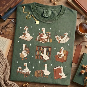 Puede incluir: Camiseta verde con un dise&ntilde;o caprichoso de gansos leyendo libros en varios escenarios. Los gansos est&aacute;n representados con gafas y accesorios, rodeados de libros y estrellas. La camiseta tiene un aspecto vintage, con el texto "Cotton Online" en la etiqueta.