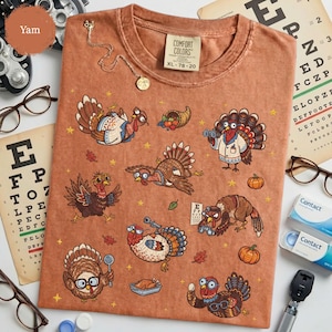 May include: A rust-colored t-shirt featuring a graphic print of multiple turkeys in various activities, including wearing glasses, holding a spoon, and using binoculars. The shirt has a Comfort Colors label indicating size XL 78-20.
