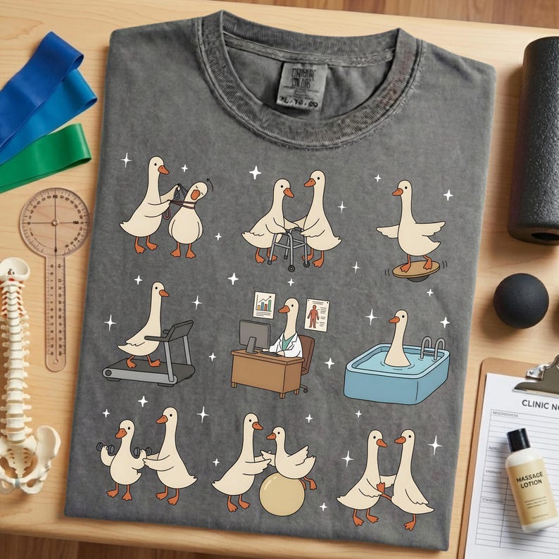 Pode incluir: Camiseta cinza com uma ilustra&ccedil;&atilde;o l&uacute;dica de gansos envolvidos em v&aacute;rias atividades de fisioterapia. O design inclui gansos usando uma esteira, equilibrando-se e em uma piscina. A camiseta tem gola redonda e um ajuste relaxado.