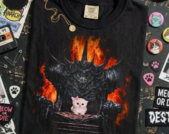 Könnte beinhalten: Ein schwarzes T-Shirt mit einem Grafikdruck eines kleinen, flauschigen, hellen Kätzchens mit einer rosa Schleife, das auf einem dunklen, verzierten, stacheligen Thron sitzt, umgeben von leuchtend orangefarbenen und roten Flammen.
