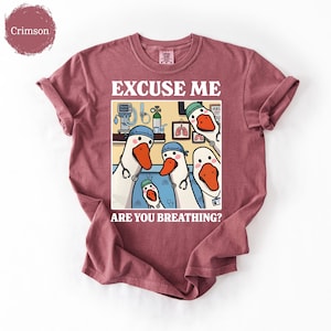 May include: Crimson-colored t-shirt featuring a cartoon illustration of geese dressed as medical professionals. The image includes the text "EXCUSE ME ARE YOU BREATHING?" in white lettering. The geese are wearing blue caps and stethoscopes.