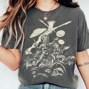 May include: Dark gray t-shirt featuring a black and white illustration of alien figures with ray guns, UFOs, and skulls. The graphic design has a vintage, comic book style.