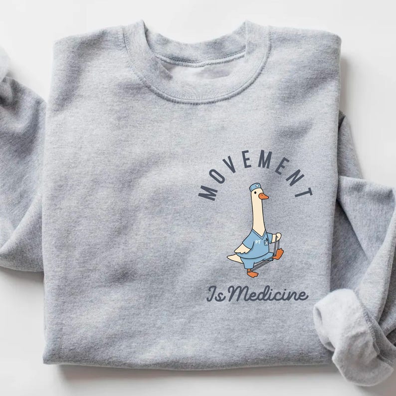 May include: A light gray sweatshirt featuring a cartoon goose in a blue medical uniform, holding a cane. The text "MOVEMENT" arches above the goose, with "Is Medicine" below. The design is centered on the chest.