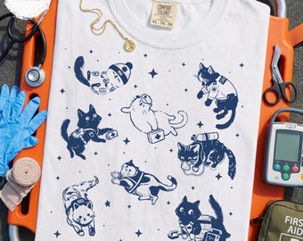 Könnte beinhalten: Weißes T-Shirt mit Rundhalsausschnitt und kurzen Ärmeln. Das Shirt zeigt eine marineblaue Illustration von Katzen in verschiedenen medizinischen Rollen. Das Shirt hat ein Comfort Colors-Etikett. Größe XL, 70-50.