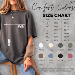 May include: A dark grey Comfort Colors t-shirt with a size chart and colour options. The size chart shows measurements in inches for sizes S to 3XL. Available colours include white, ivory, pepper, moss, espresso, blue jean, black, and crimson.