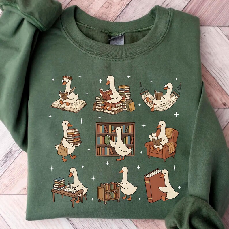 Puede incluir: Sudadera verde con un dise&ntilde;o caprichoso de gansos de dibujos animados leyendo libros. Los gansos se representan con libros, en una hamaca y cerca de estanter&iacute;as. El dise&ntilde;o incluye peque&ntilde;as estrellas blancas.