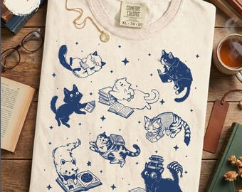 May include: Ivory Comfort Colors t-shirt with a navy blue cat and book design. The shirt features various cats reading books, with stars scattered around the design. The tag reads XL 78-20.