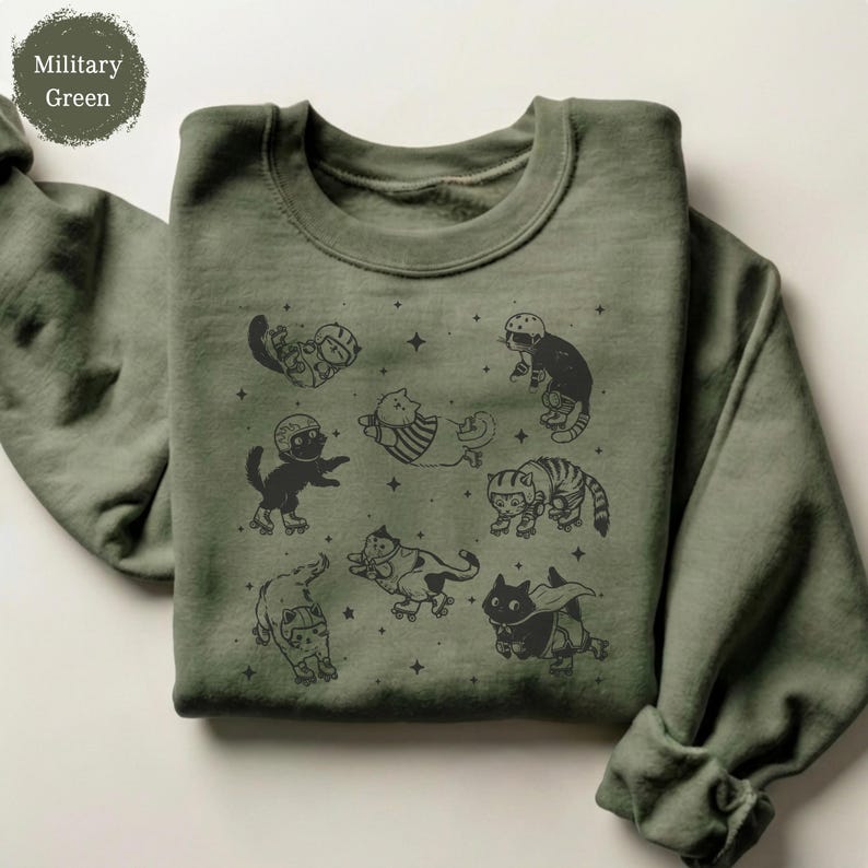 May include: Military green sweatshirt with a repeating pattern of cats in helmets and roller skates. The cats are depicted in different poses, with stars dotted around. The sweatshirt is made of a soft fabric.