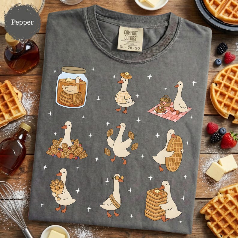 May include: Dark gray Comfort Colors t-shirt with a whimsical design of cartoon geese interacting with waffles and syrup. The shirt features the text "Pepper" and the size XL 78-20.