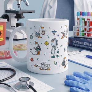 May include: A white ceramic mug featuring a repeating pattern of cartoon ducks dressed as medical professionals, including ducks in lab coats, hazmat suits, and carrying medical supplies, interspersed with small colorful virus and bacteria icons.