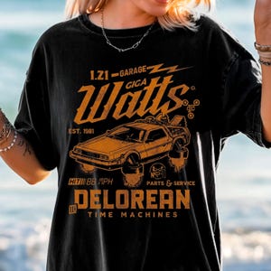 May include: Black t-shirt with a distressed orange graphic featuring a DeLorean car, lightning bolts, and the text "1.21-GARAGE-GIGA Watts EST. 1981". The shirt also says "HIT 88 MPH" and "DELOREAN TIME MACHINES".