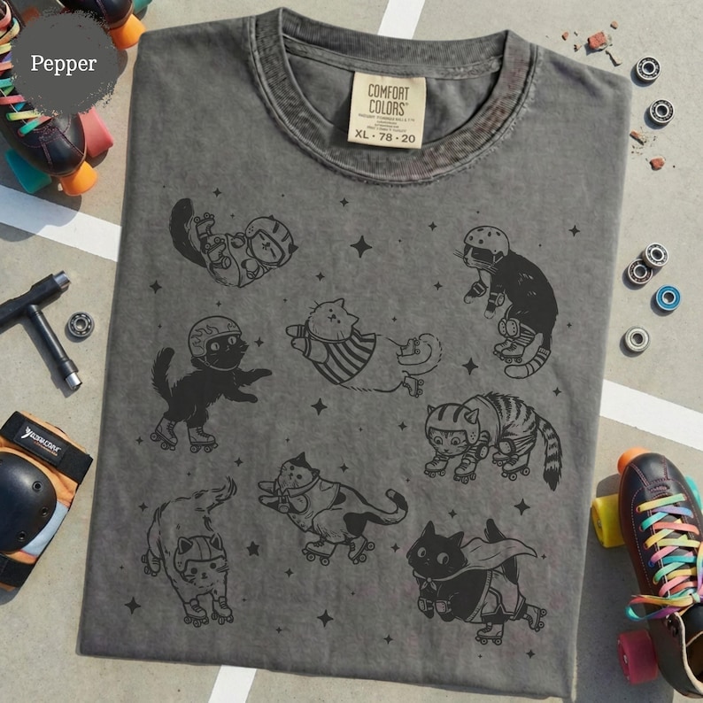 May include: A grey Comfort Colors t-shirt with a fun design of cats on roller skates. The cats are shown in different poses, wearing helmets and protective gear. The shirt has a vintage appearance, with the size XL 78-20 printed on the label.