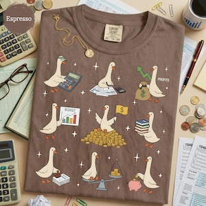May include: A brown t-shirt featuring a graphic print of white geese performing various financial tasks, including using a calculator, holding a budget chart, carrying a money bag labeled profits, and sitting on a pile of gold coins.