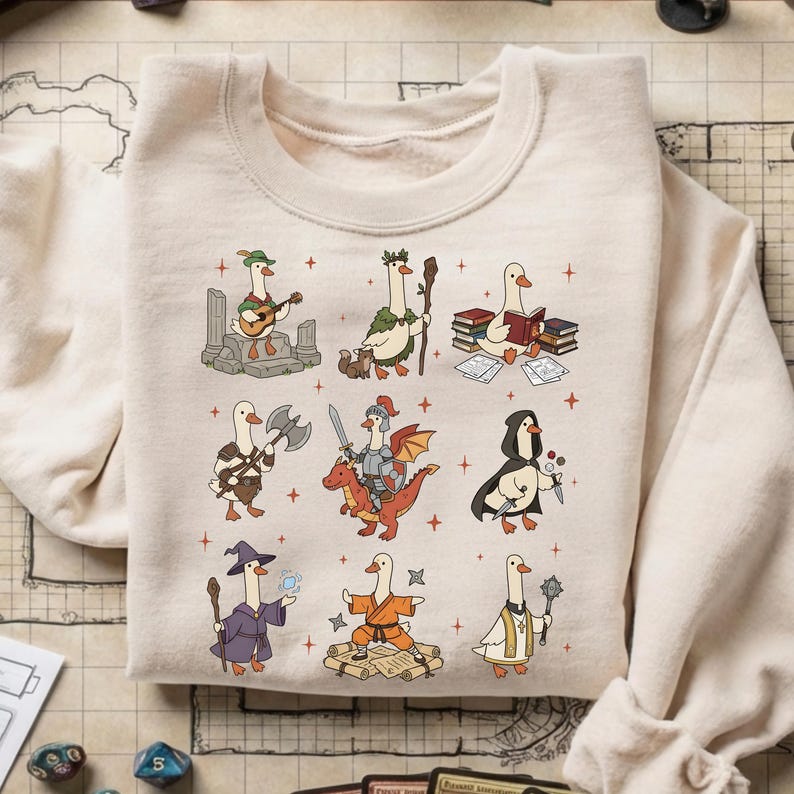 May include: Cream-colored sweatshirt featuring a whimsical design of cartoon geese in various fantasy roles. The geese are depicted as a bard, druid, scholar, warrior, knight, rogue, wizard, monk, and cleric. The design includes small red crosses.