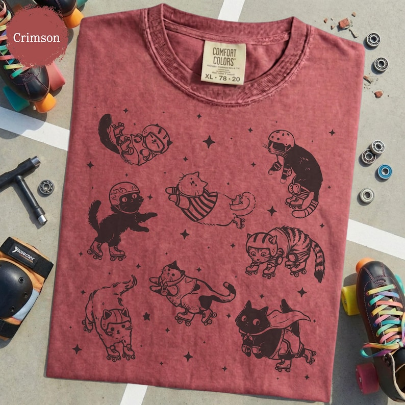 May include: Crimson t-shirt with a fun design of cats roller-skating. The cats are shown in different poses, wearing helmets and protective gear. The shirt has a classic crew neck and a tag that reads "Comfort Colors XL 78-20".