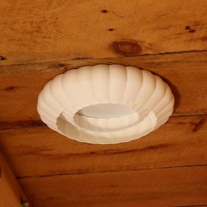 This is a white, 3d printed light shade that mounts onto 6 inch recessed lights. It diffuses the light beautifully, changing the harsh overhead light of recessed lighting into a soft glow, and provides a beautiful decorative touch as well. It has an elegant, scalloped edge and which has floral feeling to it. No hardware is needed to install the light, it comes with easy-to-install tabs that make install or changing a bulb simple.