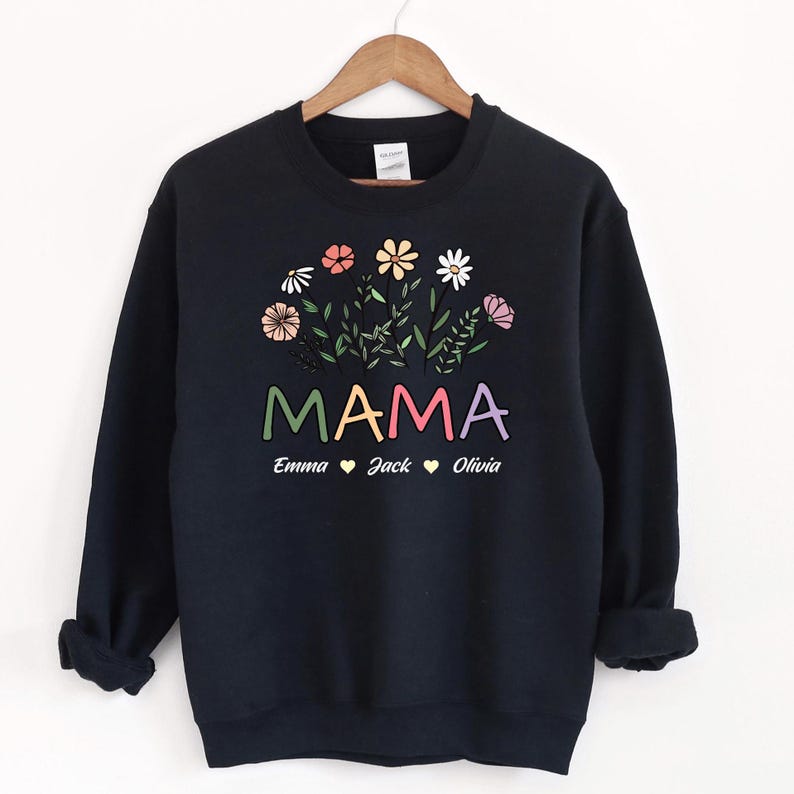 May include: Black sweatshirt featuring a floral design and the word "MAMA" in rainbow colours. Below the word "MAMA" are the names "Emma", "Jack", and "Olivia" with hearts between each name.