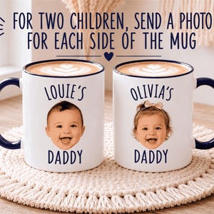 May include: Two white ceramic mugs with dark blue handles and rims, each filled with coffee featuring latte art. The mugs display the text "LOUIE'S DADDY" and "OLIVIA'S DADDY" above photographic portraits of two smiling infants.