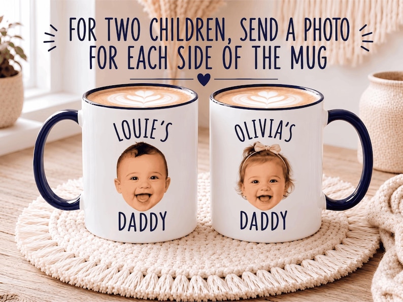 May include: Two white ceramic mugs with dark blue handles and rims, each filled with coffee featuring latte art. The mugs display the text "LOUIE'S DADDY" and "OLIVIA'S DADDY" above photographic portraits of two smiling infants.