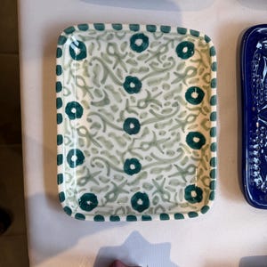 May include: A rectangular ceramic tray featuring a white base with a hand-painted pattern of light green swirling vines and dark teal circular flower motifs. The rim is decorated with a repeating border of dark teal dots on a white background.