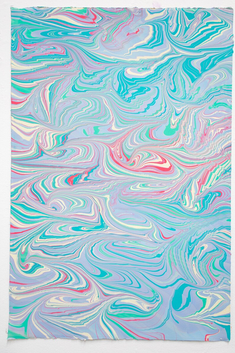 May include: Abstract art print with a marbled design. The artwork features swirling patterns in shades of blue, teal, pink, and white. The paper has a textured appearance, with visible edges. The overall aesthetic is reminiscent of water or clouds.