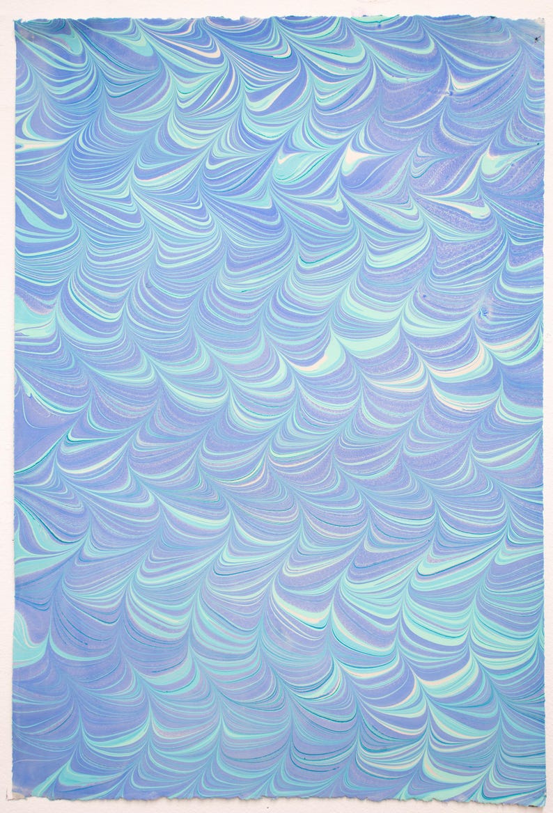 May include: A rectangular sheet of paper with a marbled design. The pattern features flowing, wave-like swirls in shades of blue, teal, and white. The edges of the paper are slightly uneven, suggesting a handmade quality.