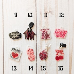 May include: A set of 10 bookish charms with various designs, including a spooky babe, a crying over book boyfriends charm, a slow burn romance reader charm, and a midnight reader charm. The charms are made of clear acrylic with black and red details.