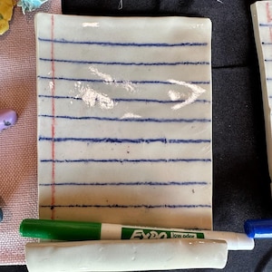 Può includere: Una tazza di ceramica bianca con manico nero e la scritta "But First, Coffee" in nero, con un carattere a mano. La tazza è su una superficie bianca.