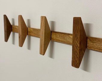 May include: A wooden wall-mounted coat rack with five triangular hooks. The rack is made of light brown wood and has a natural finish.