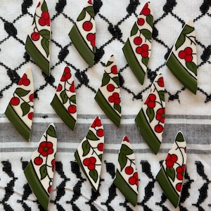 Puede incluir: Azulejos cerámicos triangulares con base blanca, con un diseño de cerezas rojas y hojas verdes. Los azulejos tienen un borde verde y están dispuestos sobre una tela estampada en blanco y negro.