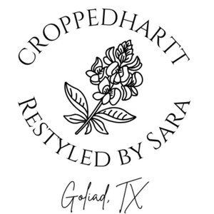May include: A black and white logo with the text "CROPPEDHARTT RESTYLED BY SARA" encircling a floral illustration. Below the circle is the text "Goliad, TX". The design is simple and elegant.
