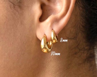 May include: Two gold hoop earrings with a smooth, polished finish. The smaller hoop is labelled 8mm and the larger hoop is labelled 10mm. These earrings feature a thick, rounded design and are worn in the earlobe, showcasing their size difference.
