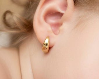 May include: A small, polished gold hoop earring with a smooth, rounded surface. The earring is a simple, thick, curved band design that sits securely on the earlobe, reflecting light with its high-shine, metallic yellow gold finish.