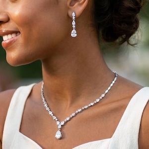 May include: A silver necklace and earring set. The necklace has small, sparkling stones leading to a pear-shaped pendant. The earrings have a similar design, with a dangling pear-shaped stone. A classic jewellery set.