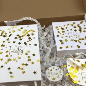 A white box with the words 'Packaging for Multiple Orders' written on it. The box is filled with white tissue paper and two white boxes. The boxes are decorated with gold stars and the words 'Trendy' and 'Free Gift'.