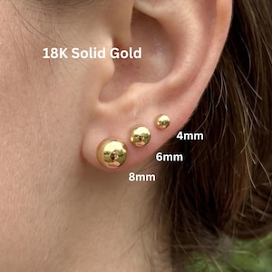 May include: Three 18K solid gold ball stud earrings in graduated sizes. The earrings are labeled with sizes 4mm, 6mm, and 8mm, showing their respective diameters as they appear arranged in a row on an earlobe.