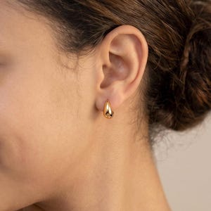 Gold-colored hoop earrings, 8mm in size, are displayed on an ear. The earrings have a smooth, polished finish and a classic, rounded shape. The image is a close-up, highlighting the jewelry's design and shine.