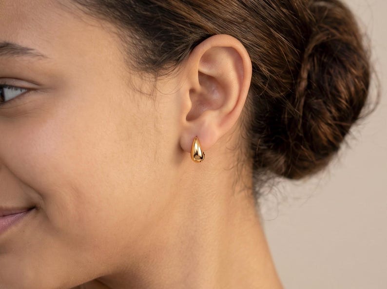 Gold-colored hoop earrings, 8mm in size, are displayed on an ear. The earrings have a smooth, polished finish and a classic, rounded shape. The image is a close-up, highlighting the jewelry's design and shine.