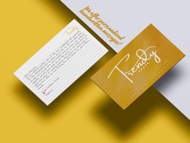 May include: A white rectangular card with lined paper and handwritten text, alongside a mustard yellow business card featuring the white script logo Trendy Adore. The text on the card includes the word Trendy and a message ending with Happy birthday, friend.