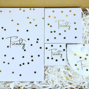 May include: A white gift box containing a large rectangular box, two square boxes, and a semi-circular pouch, all featuring the gold script text Frendy Adore and scattered gold star confetti, nestled in white shredded paper filler.